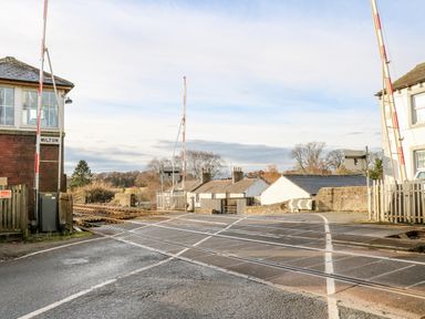 A level crossing with railway tracks and closed barriers with houses and trees in the background at The Stable Milton near Brampton