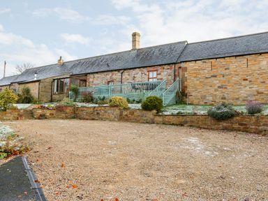 A gravel driveway leading to a stone building with a wooden deck and stairs and plants at The Stable in Milton near Brampton