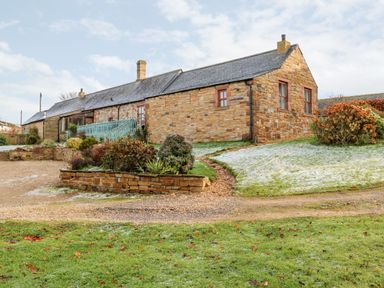 An exterior view of a stone house with a slate roof surrounded by a garden with shrubs and a gravel driveway at The Stable Milton near Brampton