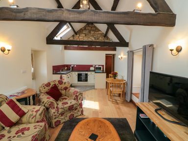 A living area with floral upholstered chairs and a wooden coffee table next to a small kitchen with a dining table and chairs at Barn Cottage High Normanby near Robin Hood's Bay
