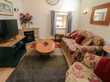 A living room with floral sofas a wooden coffee table a television and a stone fireplace at Barn Cottage in High Normanby near Robin Hood's Bay