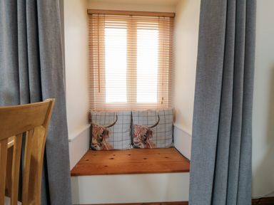 A window seat with two cushions and wooden blinds in a room with grey curtains at Barn Cottage High Normanby near Robin Hood's Bay