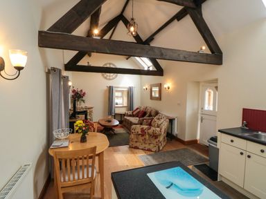 A living area with wooden ceiling beams a dining table chairs a sofa table and kitchen units at Barn Cottage in High Normanby near Robin Hoods Bay