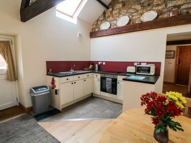 A kitchen with cabinets oven microwave and toaster a table with flowers and a stone wall at Barn Cottage High Normanby near Robin Hoods Bay