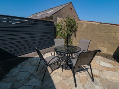 A patio with four chairs around a glass table near a stone wall and a wooden fence at Barn Cottage in High Normanby near Robin Hood's Bay