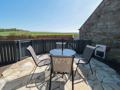 An outdoor patio area with a round glass table and four chairs next to a stone wall at Barn Cottage High Normanby near Robin Hood's Bay