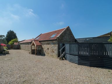 Stone building with tiled roof skylights and black wooden fence on gravel ground at Barn Cottage High Normanby near Robin Hoods Bay