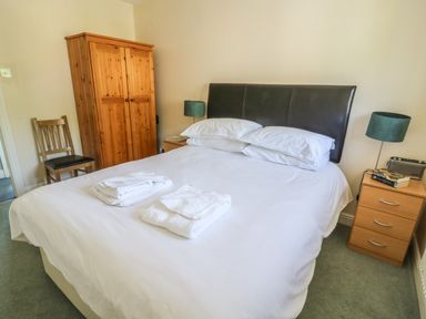 A bedroom with a double bed folded towels on the bed a wooden wardrobe chair and bedside tables at Bramble Cottage in Sedbergh