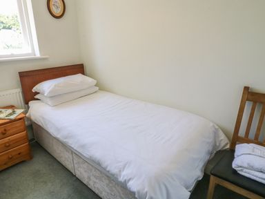 A small bedroom with a single bed wooden headboard bedside table with books wooden chair with towels on it at Bramble Cottage in Sedbergh