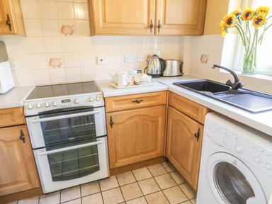 A kitchen with wooden cabinets a stove kettle toaster sink washing machine and sunflowers in a vase at Bramble Cottage in Sedbergh