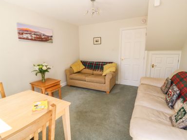 A living room with sofas a wooden table with a book and flowers on a side table at Bramble Cottage in Sedbergh