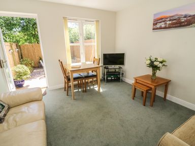 A living room with a dining table and chairs a television and side tables with flowers at Bramble Cottage in Sedbergh