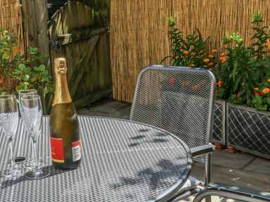 An outdoor metal table with a bottle of champagne and three empty glasses near a metal chair and plants at Bramble Cottage in Sedbergh