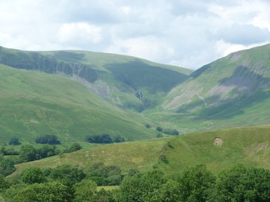 Green hills and valleys with scattered trees under a cloudy sky in Sedbergh