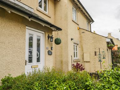 The exterior of a beige house with a white door and windows with plants in front at Bramble Cottage Sedbergh