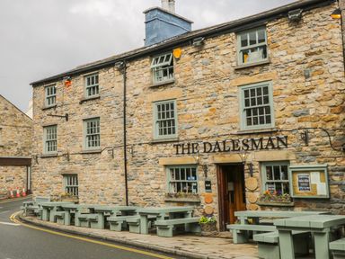 An exterior view of a stone building with green framed windows and outdoor seating at The Dalesman