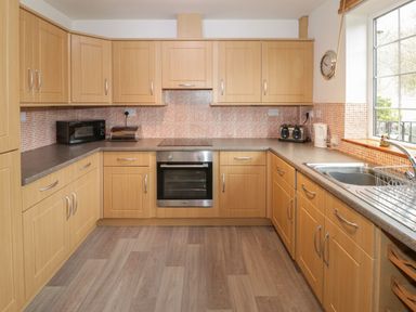 A kitchen with wooden cabinets a microwave toaster kettle oven and a sink at No 1 Railway Cottages in Betws-y-Coed