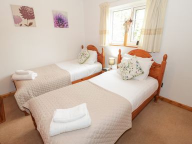 A bedroom with two single wooden beds with beige blankets and floral cushions at No 1 Railway Cottages in Betws-y-Coed