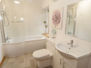 A bathroom with a bathtub shower combination a toilet a sink with storage cabinets a mirror and a flower picture at No 1 Railway Cottages in Betws-y-Coed