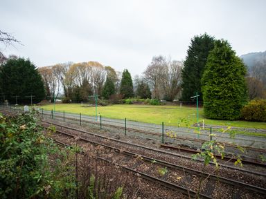 Railway tracks with a gravel path and grass area surrounded by trees at No 1 Railway Cottages in Betws-y-Coed