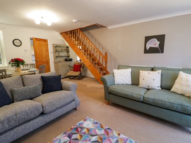 A living room with two sofas pillows a colorful rug wooden staircase and a rocking chair at No 1 Railway Cottages in Betws-y-Coed