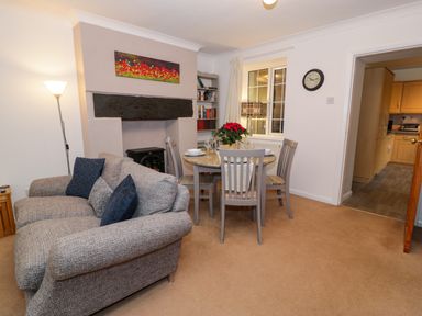 A living room with gray sofa and dining table with chairs next to a window and door to kitchen at No 1 Railway Cottages in Betws-y-Coed