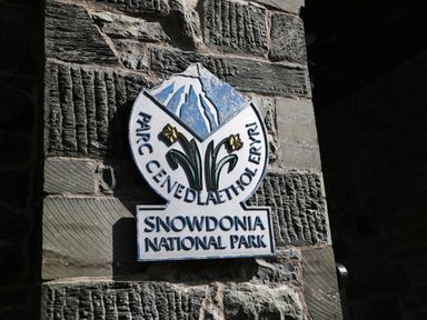 A stone wall with a Snowdonia National Park sign with Welsh text and mountain and flower images at No 1 Railway Cottages in Betws-y-Coed