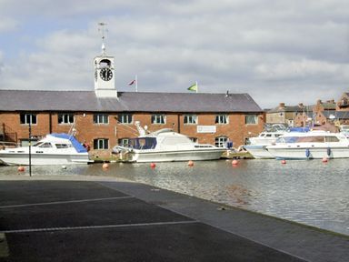 Boats docked in front of a brick building with a clock tower near a waterfront