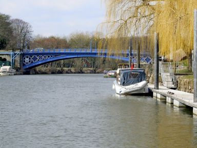 A river with boats moored next to a dock and a blue metal bridge in the background at Rosewaters Cottage in Astley Burf near Stourport-on-Severn
