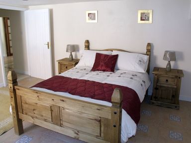 A bedroom with a wooden bed and matching bedside tables with lamps at Rosewaters Cottage in Astley Burf near Stourport-on-Severn