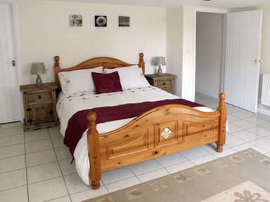 A bedroom with a wooden bed, two bedside tables with lamps, artwork above the bed at Rosewaters Cottage in Astley Burf near Stourport-on-Severn