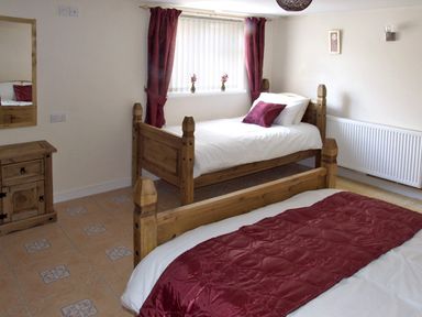 A bedroom with two wooden beds with white bedding and red accents at Rosewaters Cottage in Astley Burf near Stourport-on-Severn