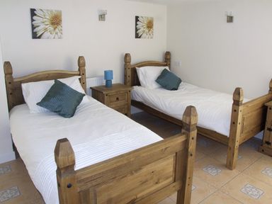 A bedroom with two wooden single beds white bedding blue pillows a wooden nightstand with a blue lamp and flower pictures on the wall at Rosewaters Cottage in Astley Burf near Stourport-on-Severn