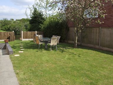 A garden with lawn chairs around a table and a tree near a brick house at Rosewaters Cottage in Astley Burf near Stourport-on-Severn