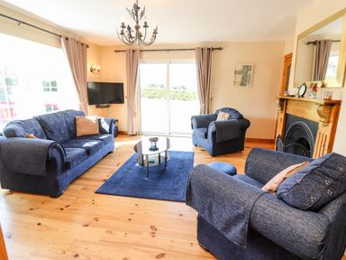 A living room with blue sofas a glass coffee table a fireplace and a wall-mounted television at Fern View House Beaufort near Killorglin County Kerry