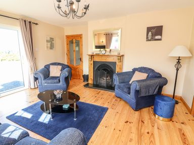 A living room with blue armchairs a glass coffee table a fireplace and wooden floor at Fern View House in Beaufort near Killorglin County Kerry