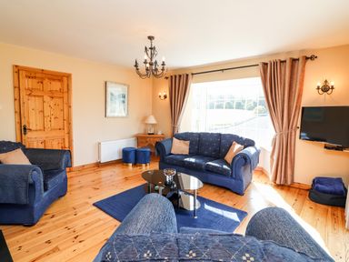 A living room with blue sofas a glass coffee table wooden floor wooden door and a mounted TV at Fern View House in Beaufort near Killorglin County Kerry