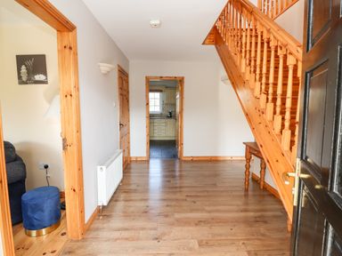 An entryway with wood flooring and staircase a doorway to a kitchen and a partially visible living room at Fern View House in Beaufort near Killorglin County Kerry