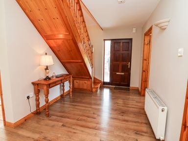 A hallway with a wooden staircase a wooden door a console table with a lamp and a radiator at Fern View House in Beaufort near Killorglin County Kerry