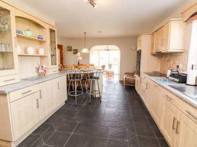 A kitchen with wooden cabinets a countertop two bar stools and a dining table at Fern View House Beaufort near Killorglin County Kerry