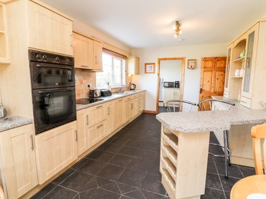 A kitchen with light wood cabinets a black oven a window and a countertop with stools at Fern View House in Beaufort near Killorglin County Kerry