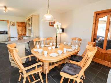 A dining area with a wooden table set with dishes and cups and wooden chairs with cushions at Fern View House in Beaufort near Killorglin County Kerry