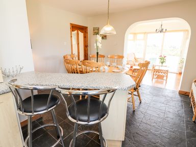 A kitchen with bar stools and a dining area with wooden chairs and a table at Fern View House in Beaufort near Killorglin County Kerry