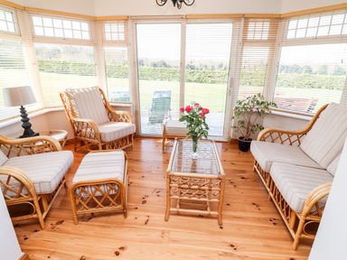A sunroom with rattan furniture a glass top table and flowers on the table at Fern View House Beaufort near Killorglin County Kerry