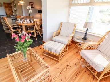 A sitting area with striped cushioned chairs a glass coffee table with flowers and a dining table with chairs in the background at Fern View House in Beaufort near Killorglin County Kerry
