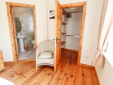 An open wooden door leading to a bathroom and another to a closet with shelves a wicker chair with a cushion on wooden floor at Fern View House in Beaufort near Killorglin County Kerry