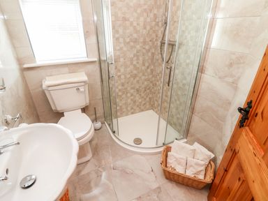 A bathroom with a toilet, sink, corner shower with glass doors, and basket of towels at Fern View House in Beaufort near Killorglin County Kerry