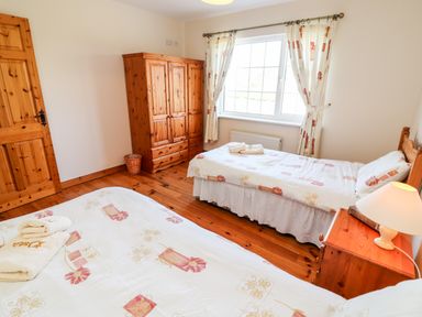 A bedroom with two single beds wooden wardrobe bedside table with lamp and window with curtains at Fern View House Beaufort near Killorglin County Kerry