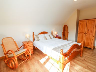 A bedroom with a wooden bed white bedding wooden rocking chair wooden wardrobes and bedside tables at Fern View House in Beaufort near Killorglin County Kerry