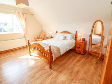A bedroom with a wooden bed bedside tables a chair and a standing mirror at Fern View House Beaufort near Killorglin County Kerry